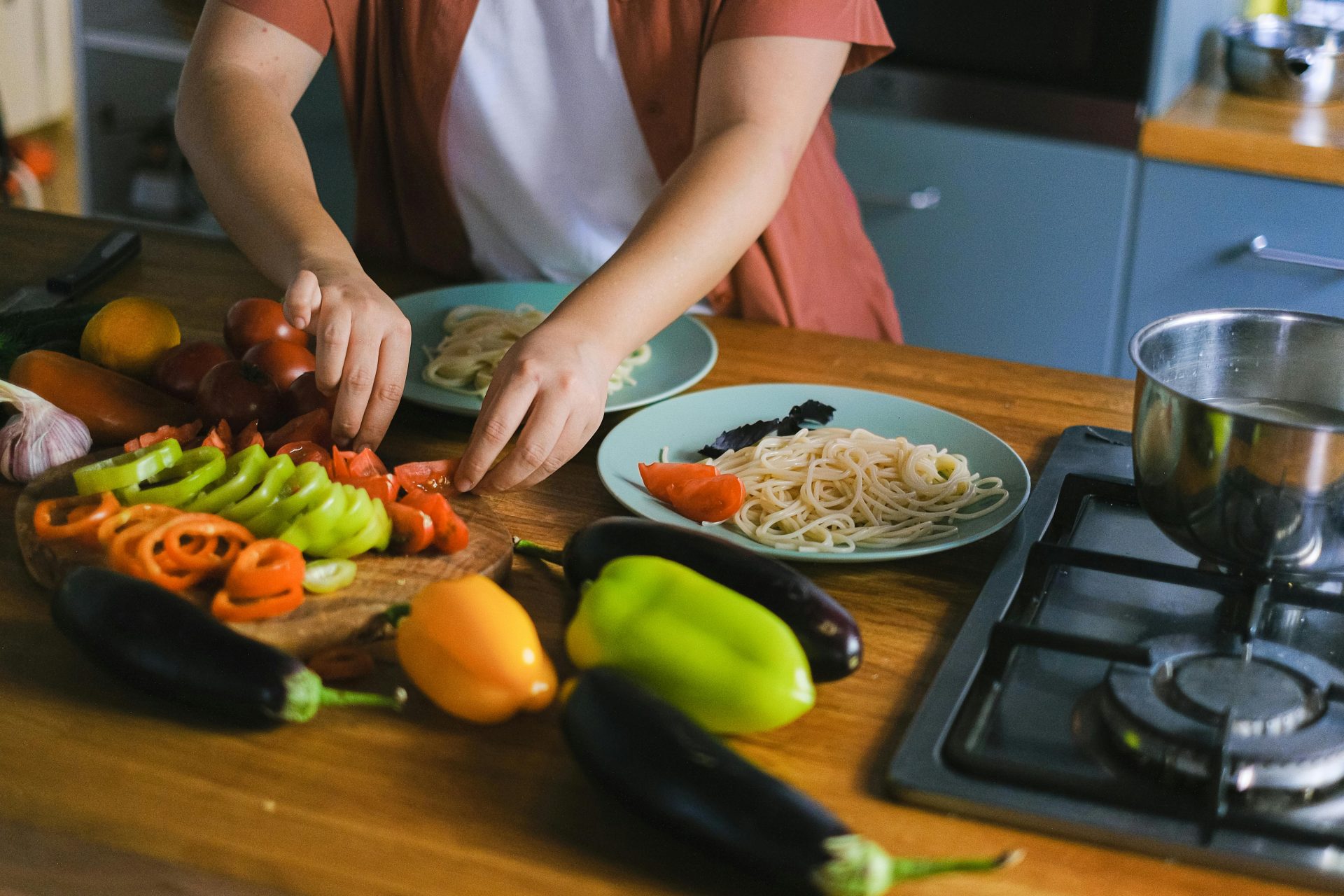Une femme dispose des légumes frais et des pâtes dans des assiettes, dans une cuisine.