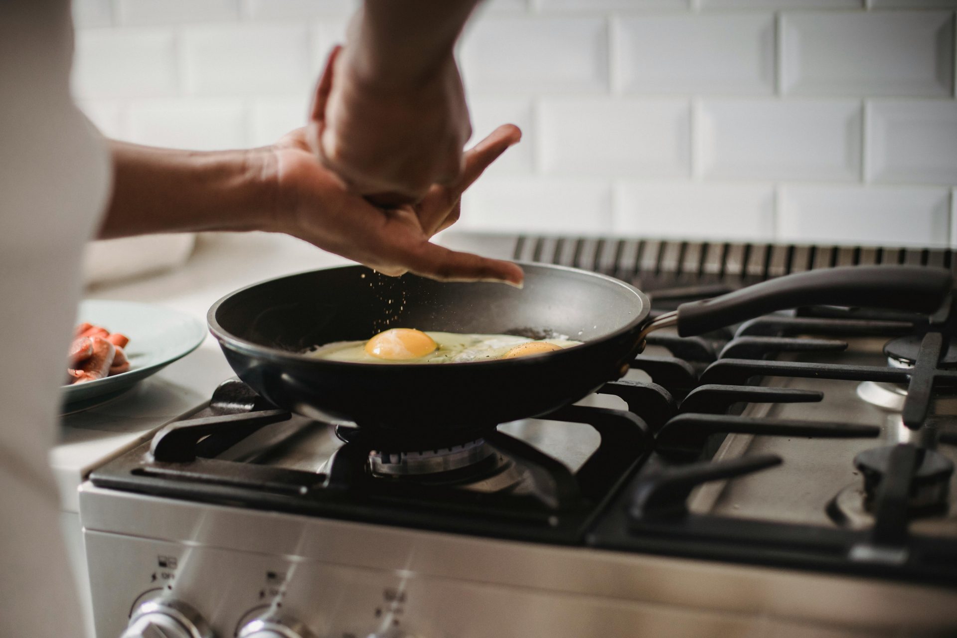 Gros plan sur des œufs en train de frire sur une cuisinière à gaz, les mains assaisonnant le plat.