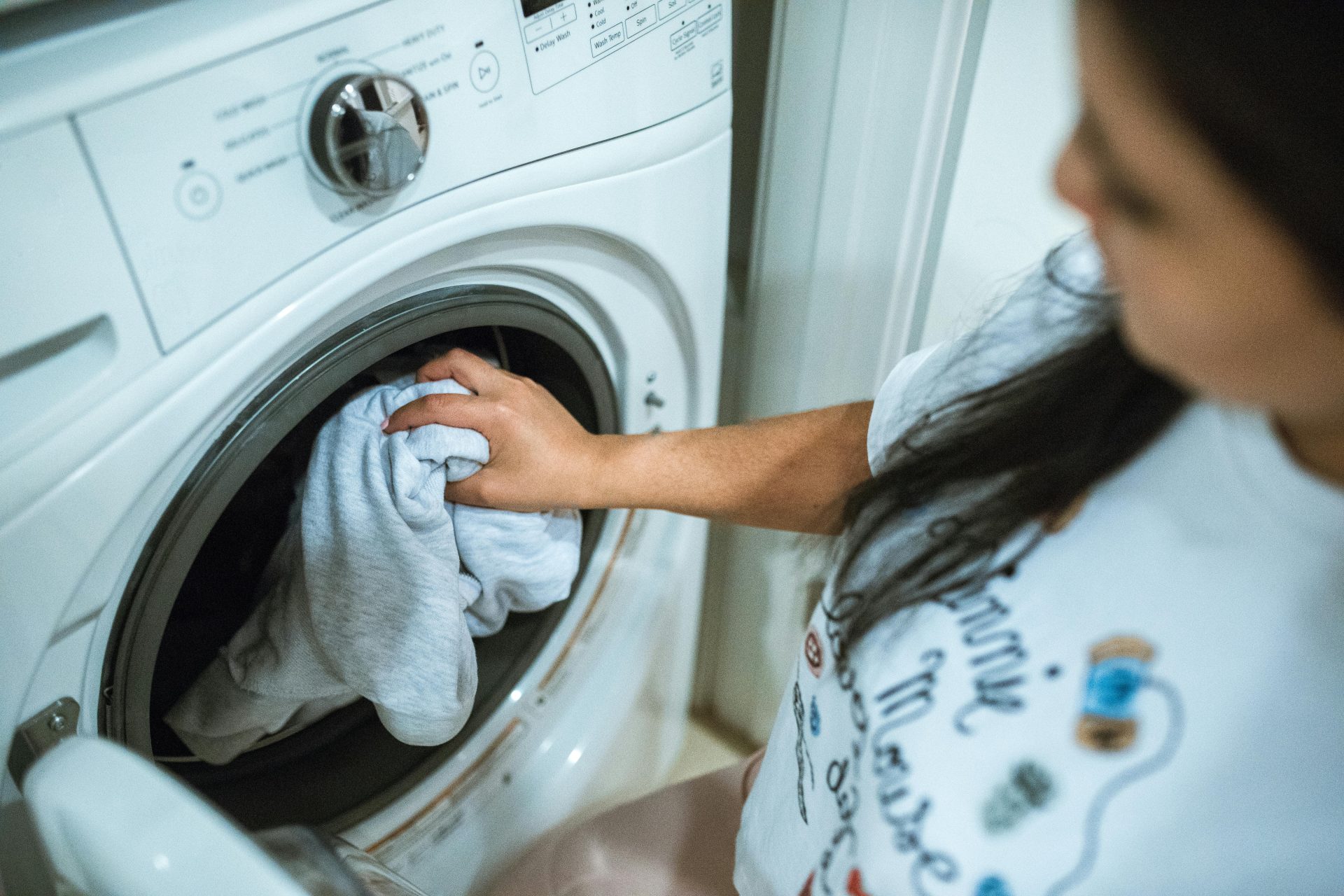 Une femme charge du linge dans une machine à laver à l'intérieur, concentrée sur ses tâches ménagères.